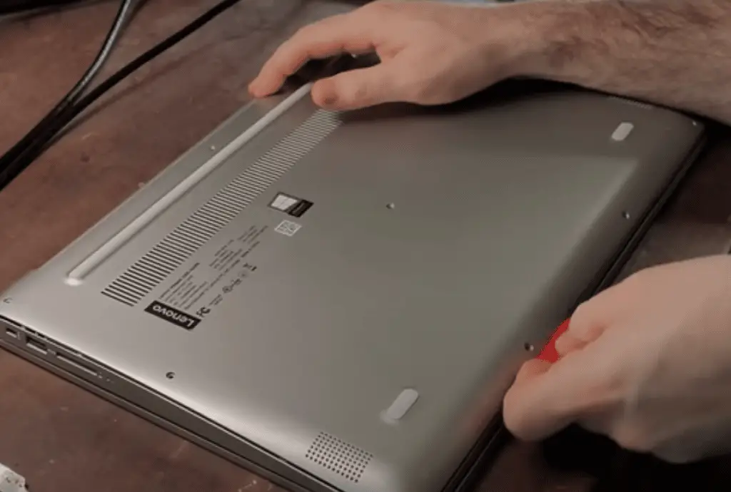 Using a plastic tool to pop off the clips from the laptop's back cover